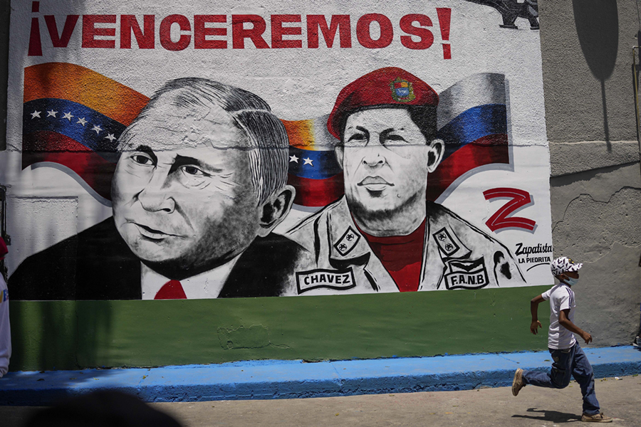 En pojke springer förbi en väggmålning med den ryske presidenten Vladimir Putin och den bortgångne presidenten Hugo Chavez, under ett evenemang för att inviga en basket- och fotbollsarena, i området Catia i Caracas, Venezuela, lördagen den 2 april 2022.