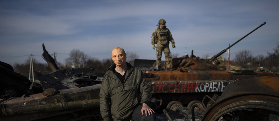 En man poserar på bilden iförd en mask av Rysslands president Vladimir Putin, medan en ukrainsk soldat står på toppen av en förstörd rysk stridsvagn i Butja, i utkanten av Kiev, Ukraina, torsdagen den 7 april 2022.
