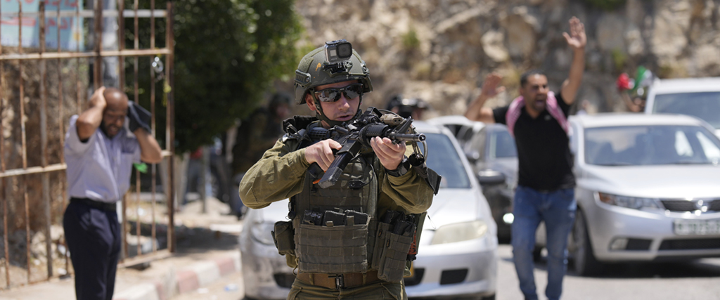  En israelisk soldat drar sitt vapen mot sörjande som deltar i begravningen av Auda Sadaqa, 17, Västbanken nära Ramallah, fredagen den 3 juni 2022.
