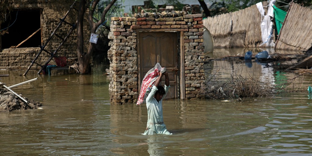 En man bär tillhörigheter från sitt översvämmade hem i Pakistan.