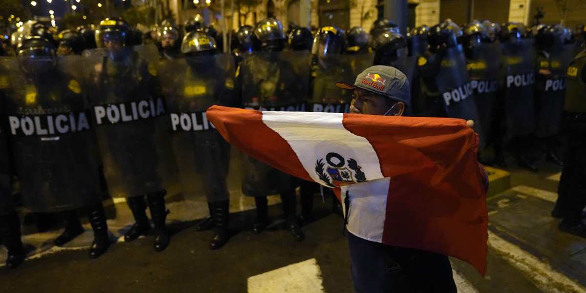 En anhängare till den avsatte peruanska presidenten Pedro Castillo håller en nationell flagga framför en avspärrning av kravallpoliser i Lima, Peru, torsdagen den 15 december 2022.