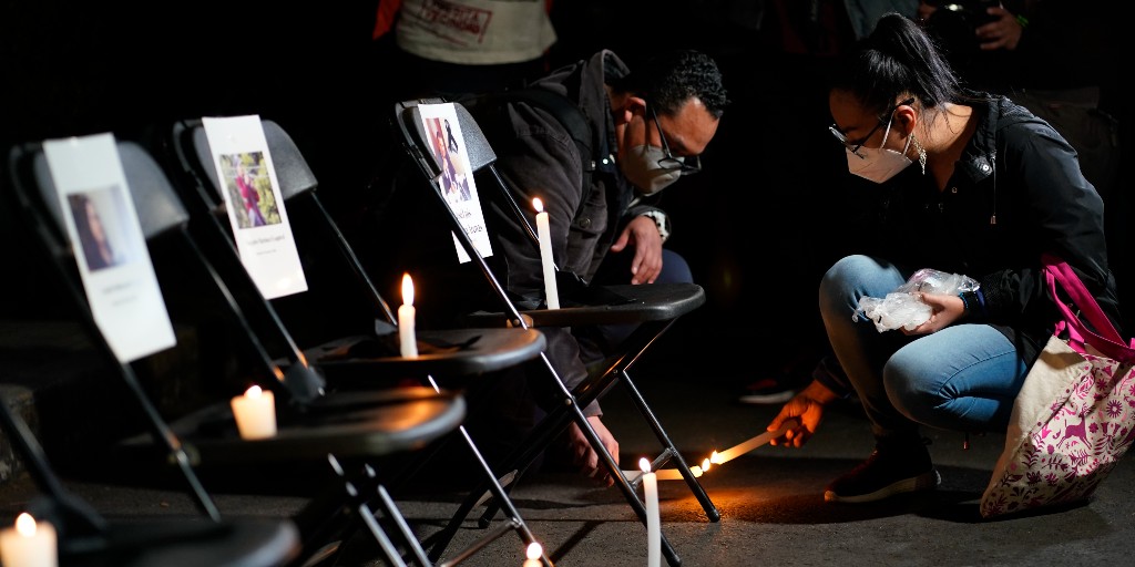 En par tänder ett ljus bredvid en rad stolar där bilder på mördade journalister har satts upp i Mexiko i februari 2022.