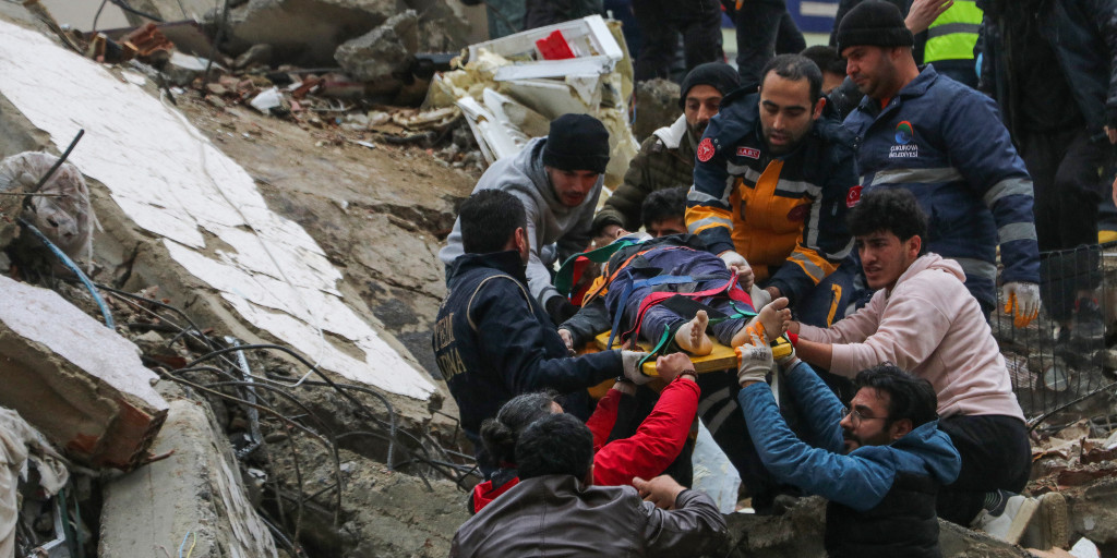 Folk hjälper räddningstjänsten att ta hand om en människa som hittats i rasmassorna av en kollapsad byggnad i Adana i Turkiet på måndagen.