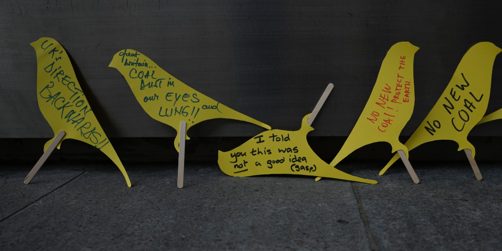 Demonstranter har skrivit budskap på små plakat föreställande gula kanariefåglar under en protest mot den nya kolgruvan i Cumbria i norra England.