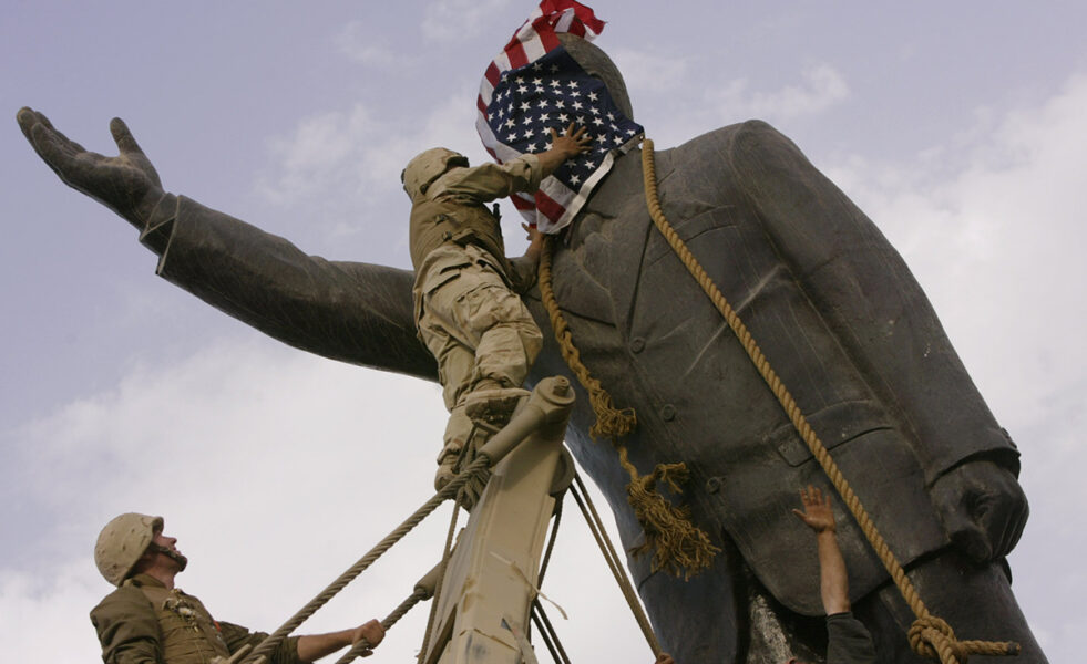 Korpral Edward Chin, från amerikanska marinen, täcker ansiktet på en staty av Saddam Hussein med en amerikansk flagga innan statyn störtades i centrala Bagdad onsdagen den 9 april 2003.
