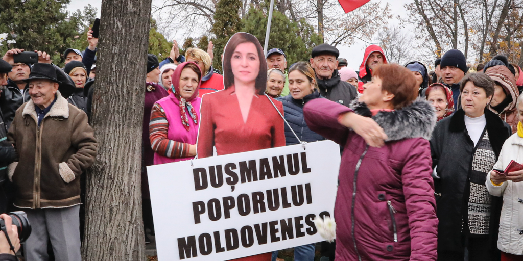 En kvinna slår en kartongmodell av Moldaviens västvänliga president Maia Sandu med en skylt som lyder "Det moldaviska folkets fiende".