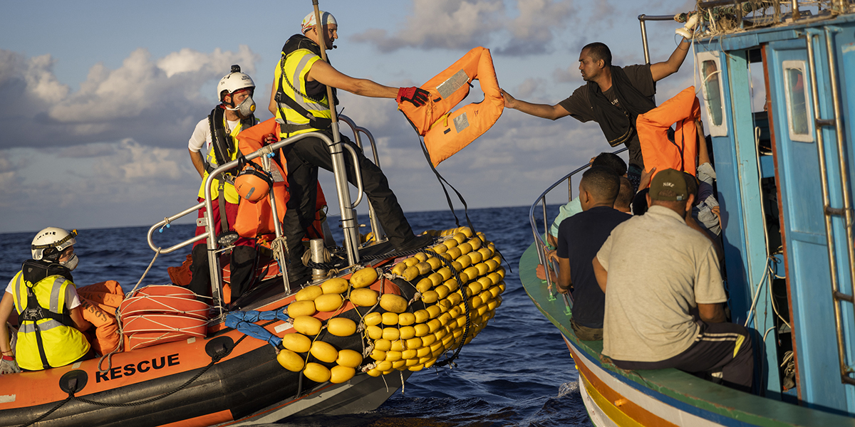 En besättningsmedlem i de icke-statliga organisationerna SOS Mediterranee och International Federation of Red Cross (IFCR) ger en skyddsjacka till en migrant torsdagen den 25 augusti 2022 i Medelhavet.