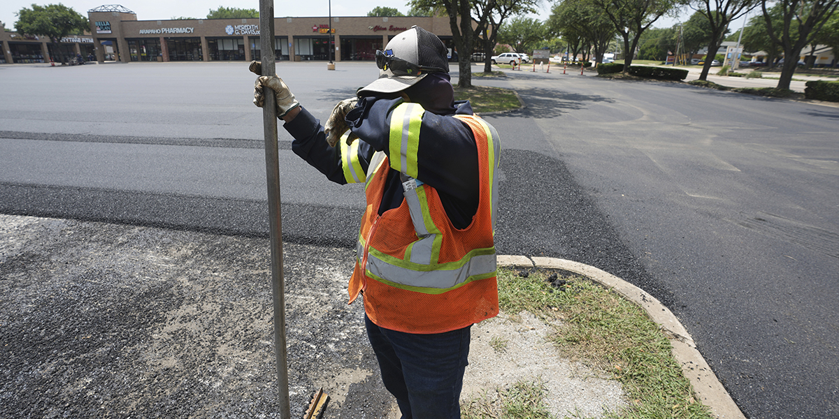 Svettigt arbete med att skotta nylagd asfalt på en parkeringsplats i Richardson, Texas, USA, tisdagen den 20 juni 2023.