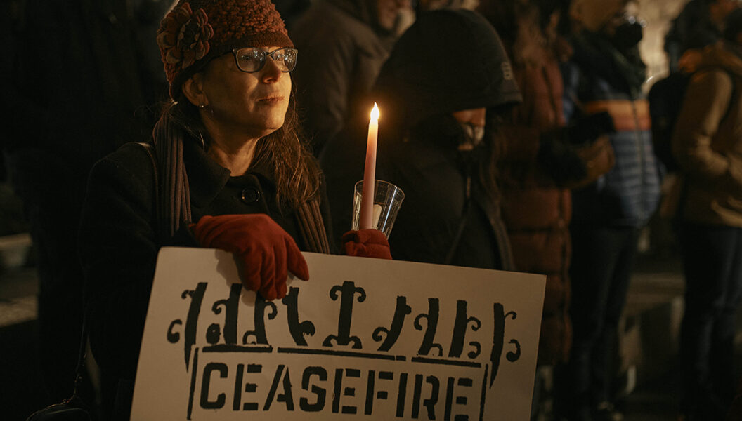 En judisk kvinna håller ett plakat och ett ljus när judiska rabbiner och medlemmar av samhället samlas och kräver en permanent vapenvila i Gaza under den första natten av den judiska högtiden Hanukkah torsdagen den 7 december 2023 i New York.