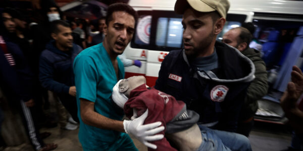 En man i läkarrock tar emot ett skadat barn som bärs av en man i keps.