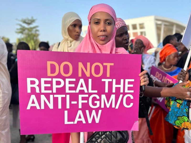 Kvinna i rosa slöja håller i rosa plakat med uppmaningen att inte häva förbud mot kvinnlig könsstympning i Gambia.