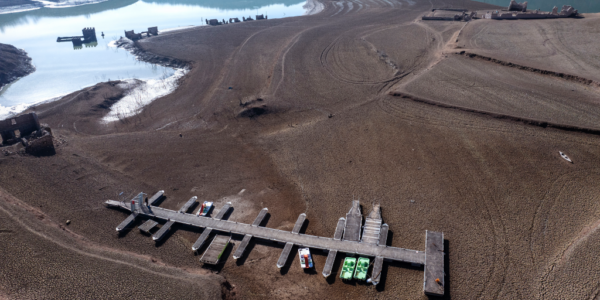 Brygga och båtar ligger torrlagda på brunt landskap.