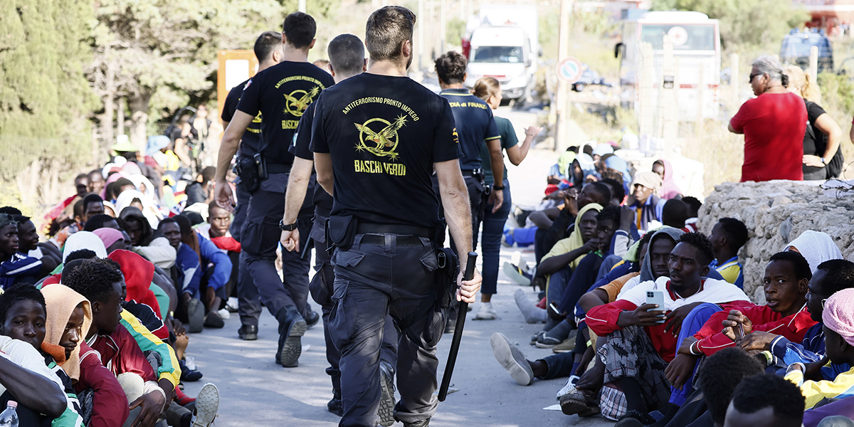 Poliser går förbi migranter på ön Lampedusa, Italien,