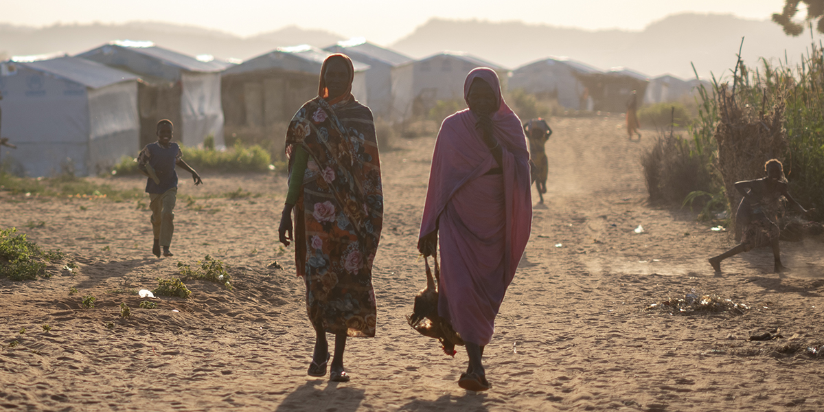 Två kvinnor vandrar i motljus i flyktingläger.