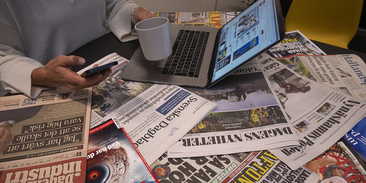 Olika nyhetstidningar och hand med kaffekopp