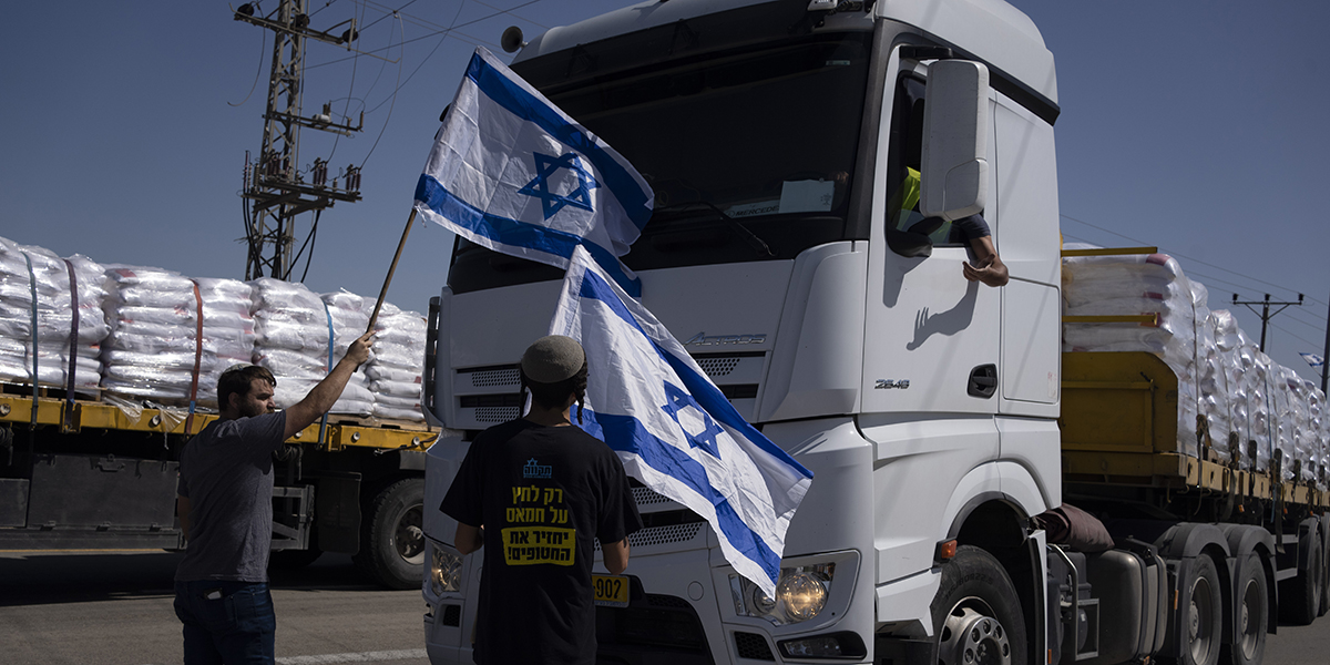 Med israeliska flaggor i händerna försöker människor stoppa lastbilar med humanitär hjälp.