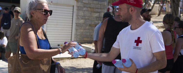En medlem av Röda Korset ger vattenflaskor till turister