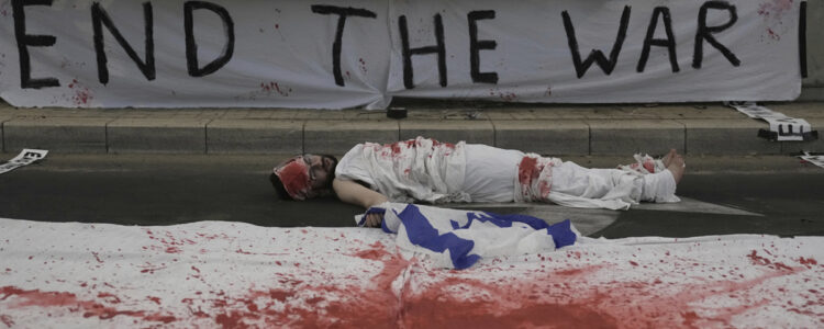 man ligger på marken vid banderoll med texten End the war
