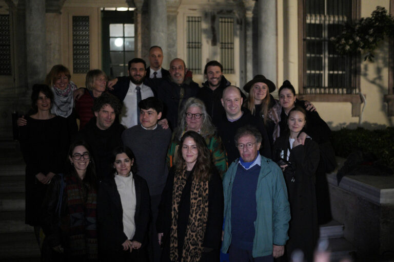 Personer står uppställda i halvmörker utanför domstol i Mytilene.