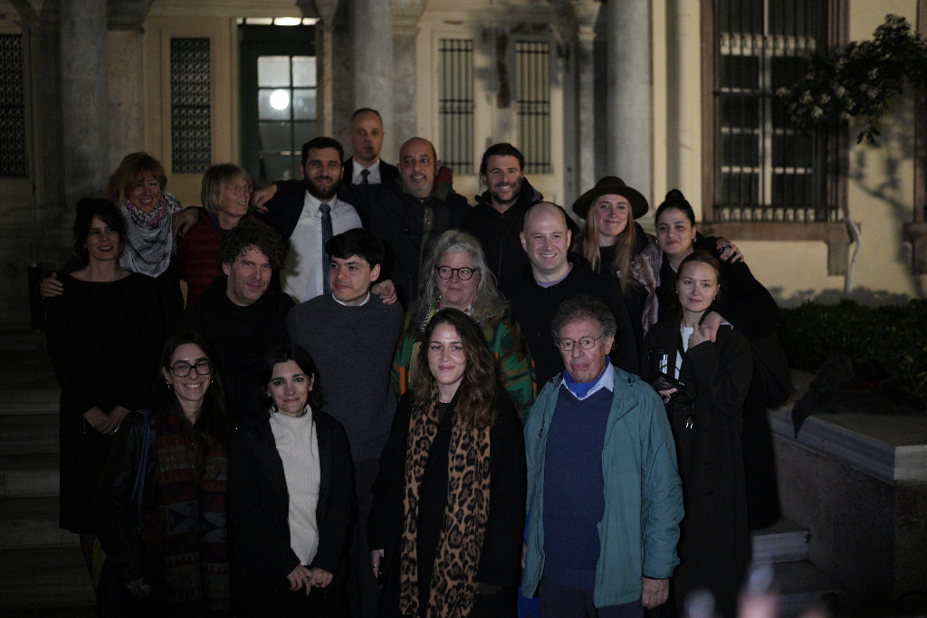 Personer står uppställda i halvmörker utanför domstol i Mytilene.