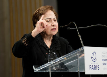 Nobels fredspristagare Shirin Ebadi i talarstol, lyfter högra handen.