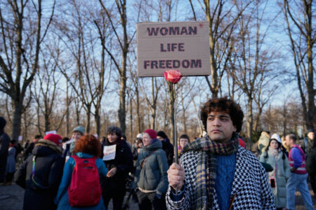 Demonstrant håller i ett plakat med texten kvinna, liv, frihet, på engelska.