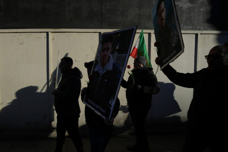 Demonstranter i London håller upp plakat på två unga män, fotade i skugga.