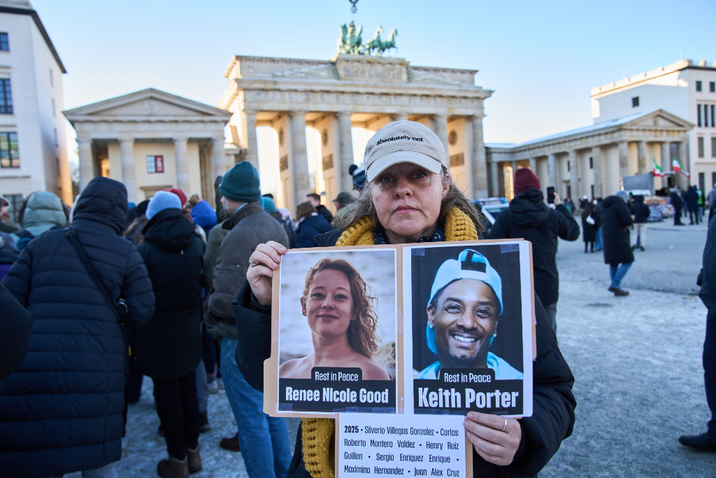 Kvinna håller upp foton på Renee Nicole Good och Keith Porter.