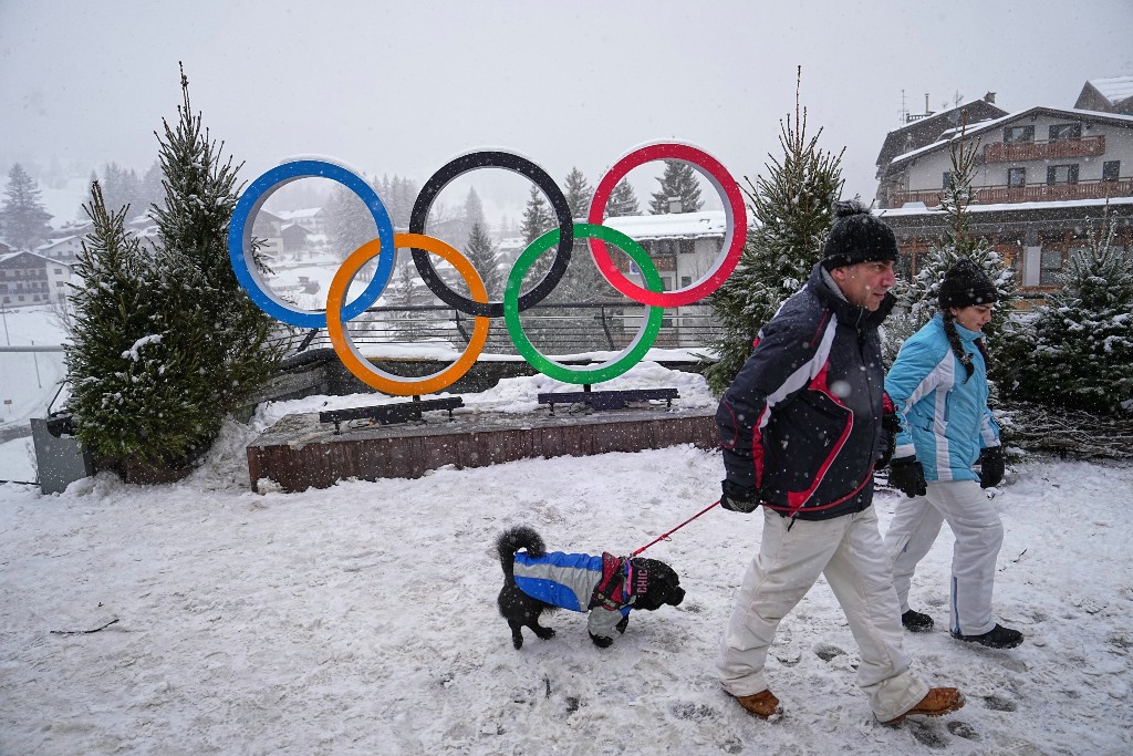 Två människor och en hund går förbi OS-ringar i snön.
