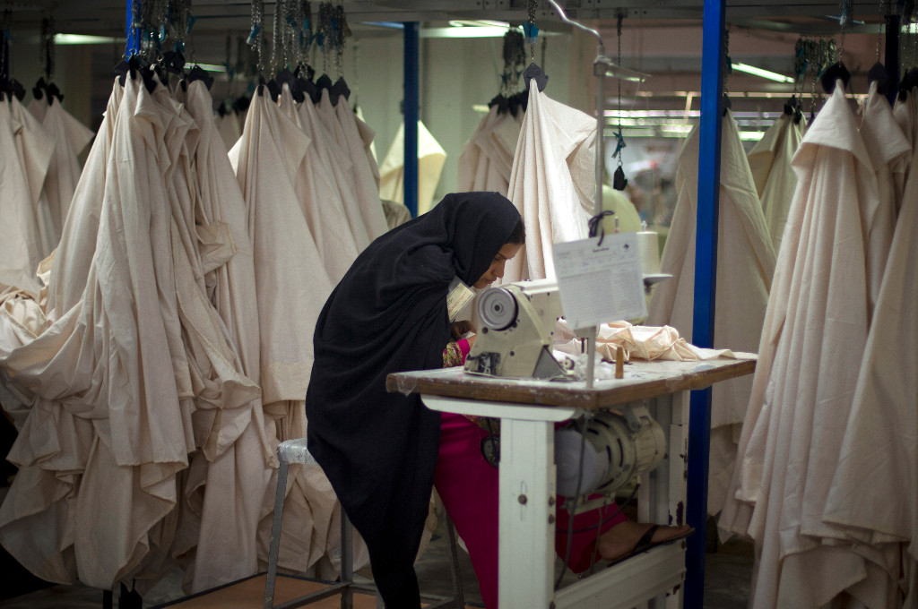 Kvinna sitter böjd över symaskin, vita lakan hänger runt omkring henne.