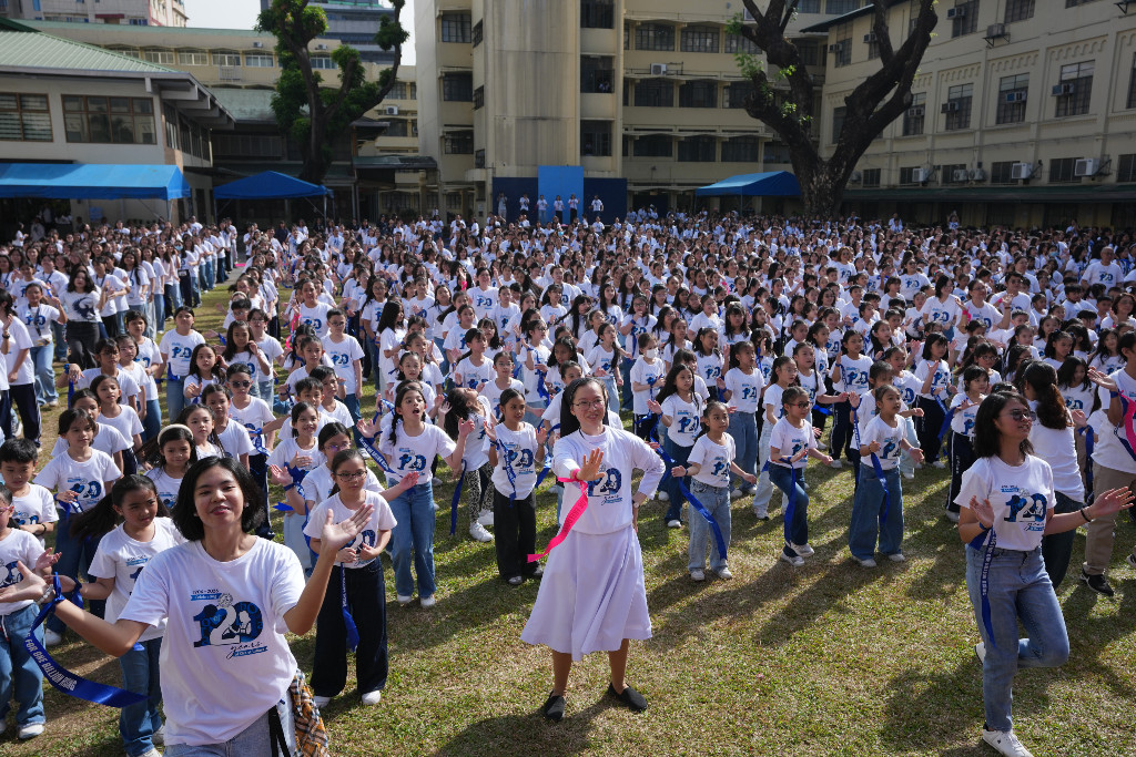 Stort antal människor, många kvinnor, dansar på gräsmatta.