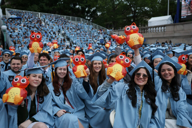 Studenter i ljusblå kappor och hattar håller upp små rödgula ugglor.