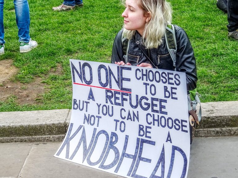 Kvinna sitter ner, håller i plakat till stöd för flyktingar.