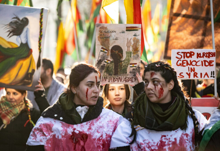 Demonstration för kurders rättigheter, i fronten två kvinnor som målat ansikte och tröjor i rött.