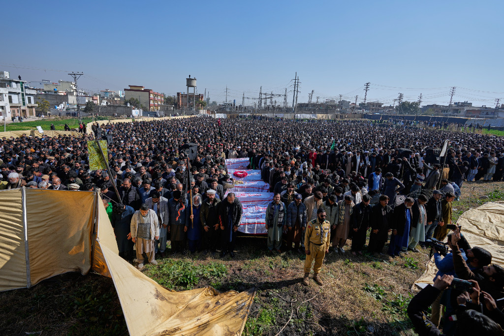 Människor deltar i en begravningsbön utomhus för flera personer som dödats i en terrorattack.