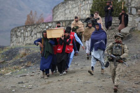 Män bär en kista i trä, en beväpnad man går bredvid.