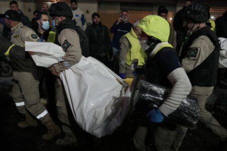 Räddningsarbetare bär död kropp i vit liksäck.