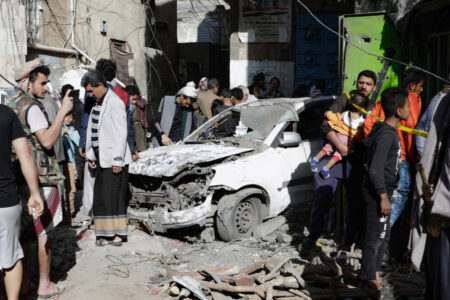 Skadad bil efter flyganfall, människor ser på.