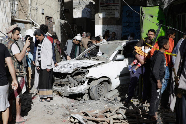 Skadad bil efter flyganfall, människor ser på.