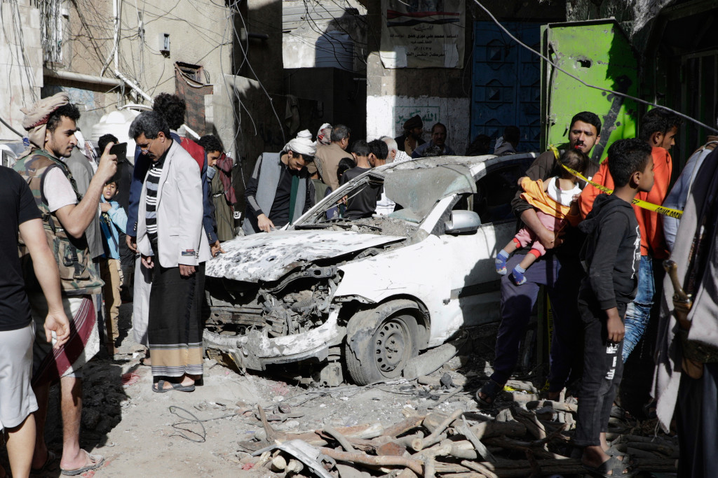 Skadad bil efter flyganfall, människor ser på.