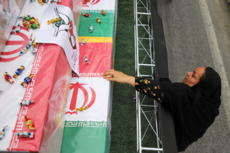 Kvinna sträcker sig mot kistor insvepta i Islamiska republikens flagga.