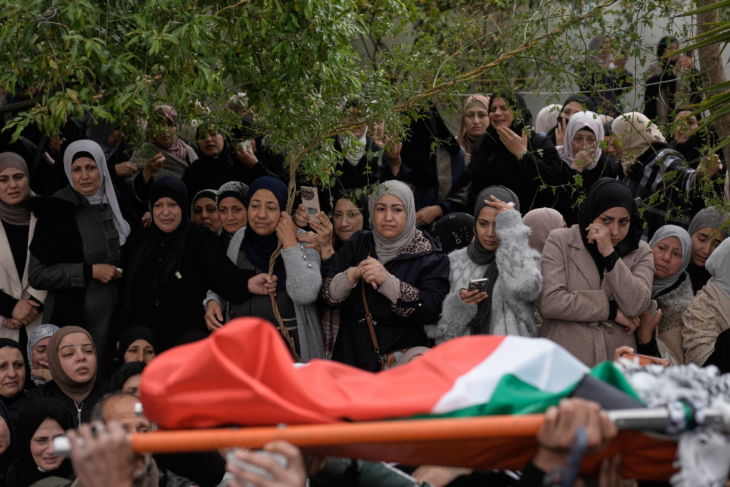 Kvinnor vid vägkanten ser hur en kista insvept i palestinska flaggan bärs förbi dem.