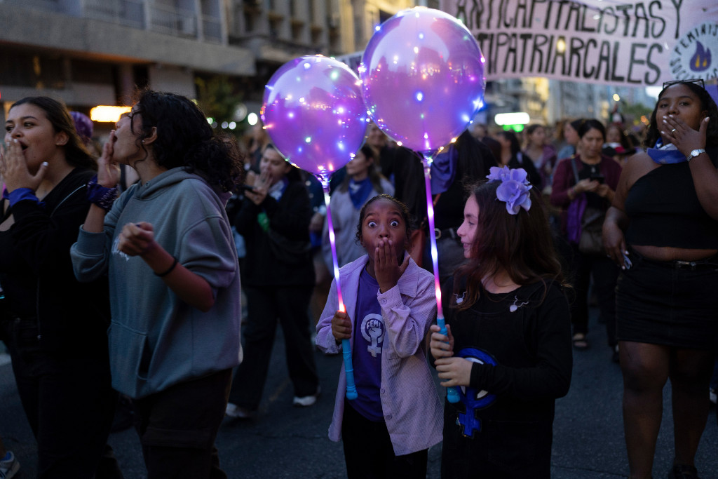 Två flickor håller i lila ballonger under en demonstration.