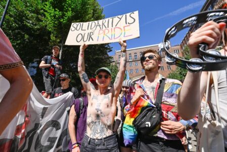 Personer med regnbågsflagga håller plakat.