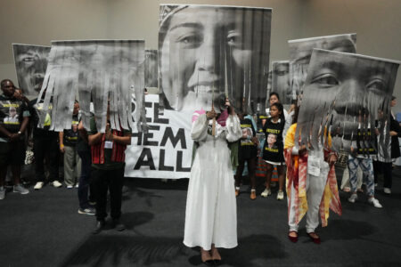 Människor protesterar, håller upp stora porträtt på gripna klimataktivister i svartvitt.