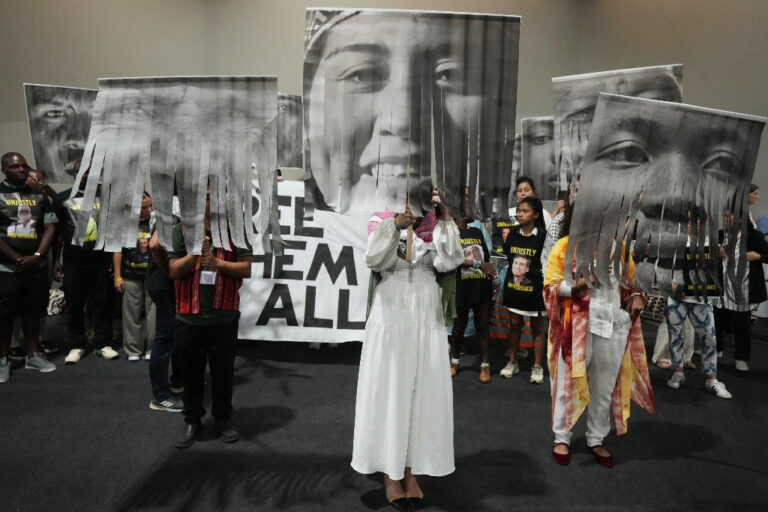 Människor protesterar, håller upp stora porträtt på gripna klimataktivister i svartvitt.
