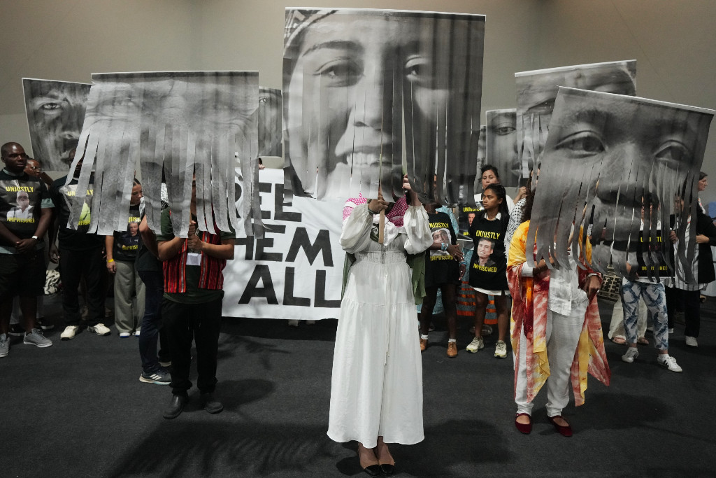 Människor protesterar, håller upp stora porträtt på gripna klimataktivister i svartvitt.