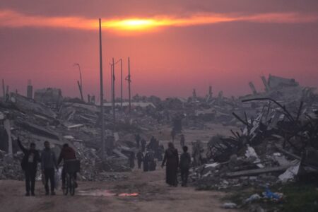 Människor går i skymningen i ett sönderbombat Gaza.