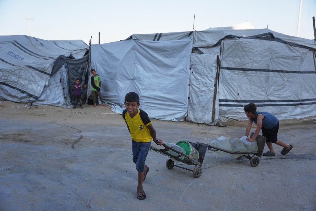 Barn i Gaza hämtar vatten, framför tält.