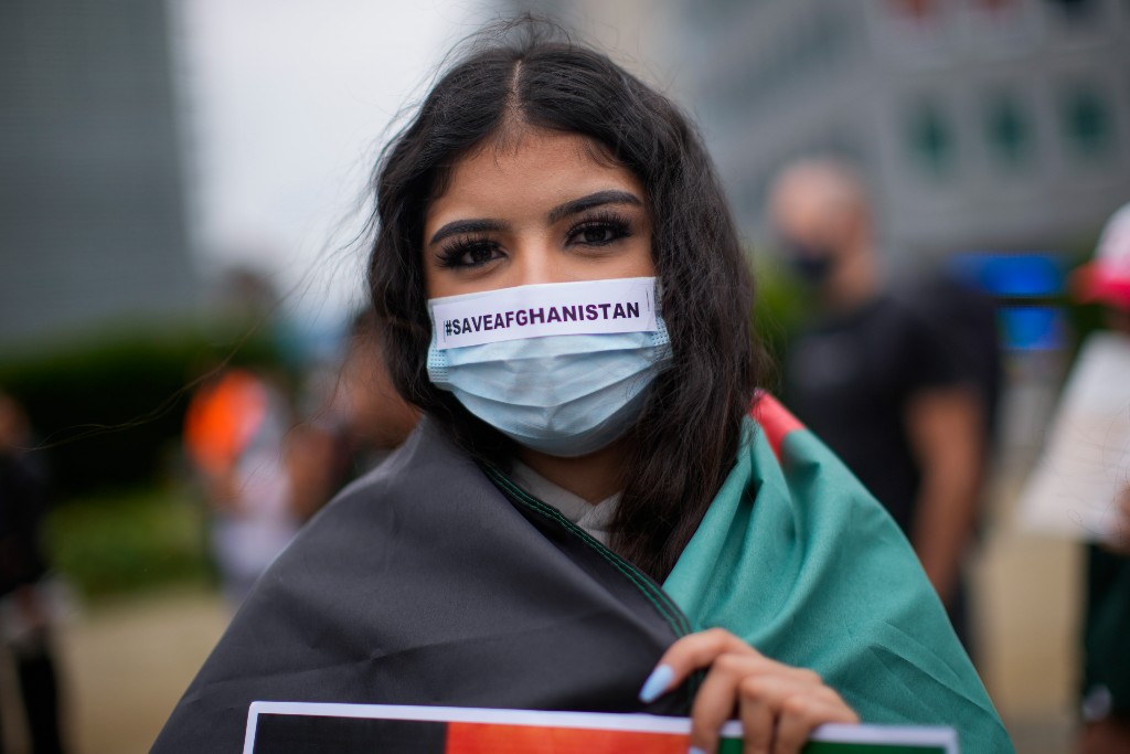 Kvinna med mask om munnen står insvept i flagga med texten rädda Afghanistan på munskyddet.